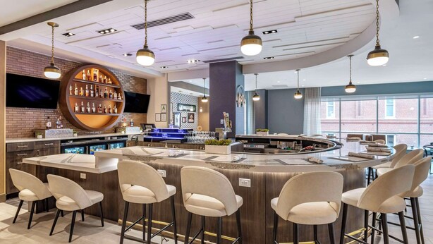A modern bar area with a circular bar, multiple seating options, and a large screen. - Cambria Hotel Louisville Downtown-Whiskey Row (Louisville)