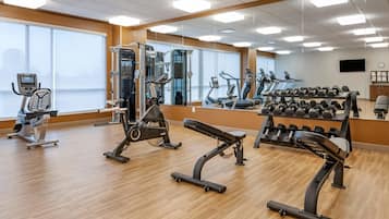 Uma academia com equipamentos de cardio, bancos de peso e halteres.