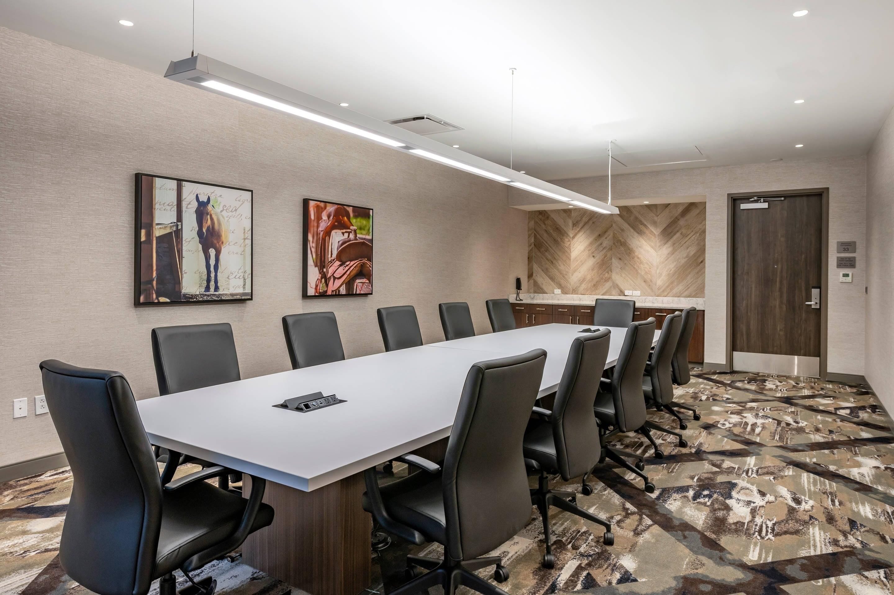 A conference room with a long table, black chairs, and two framed artworks on the wall.