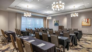 A conference room with tables and chairs, large windows, and modern chandeliers.