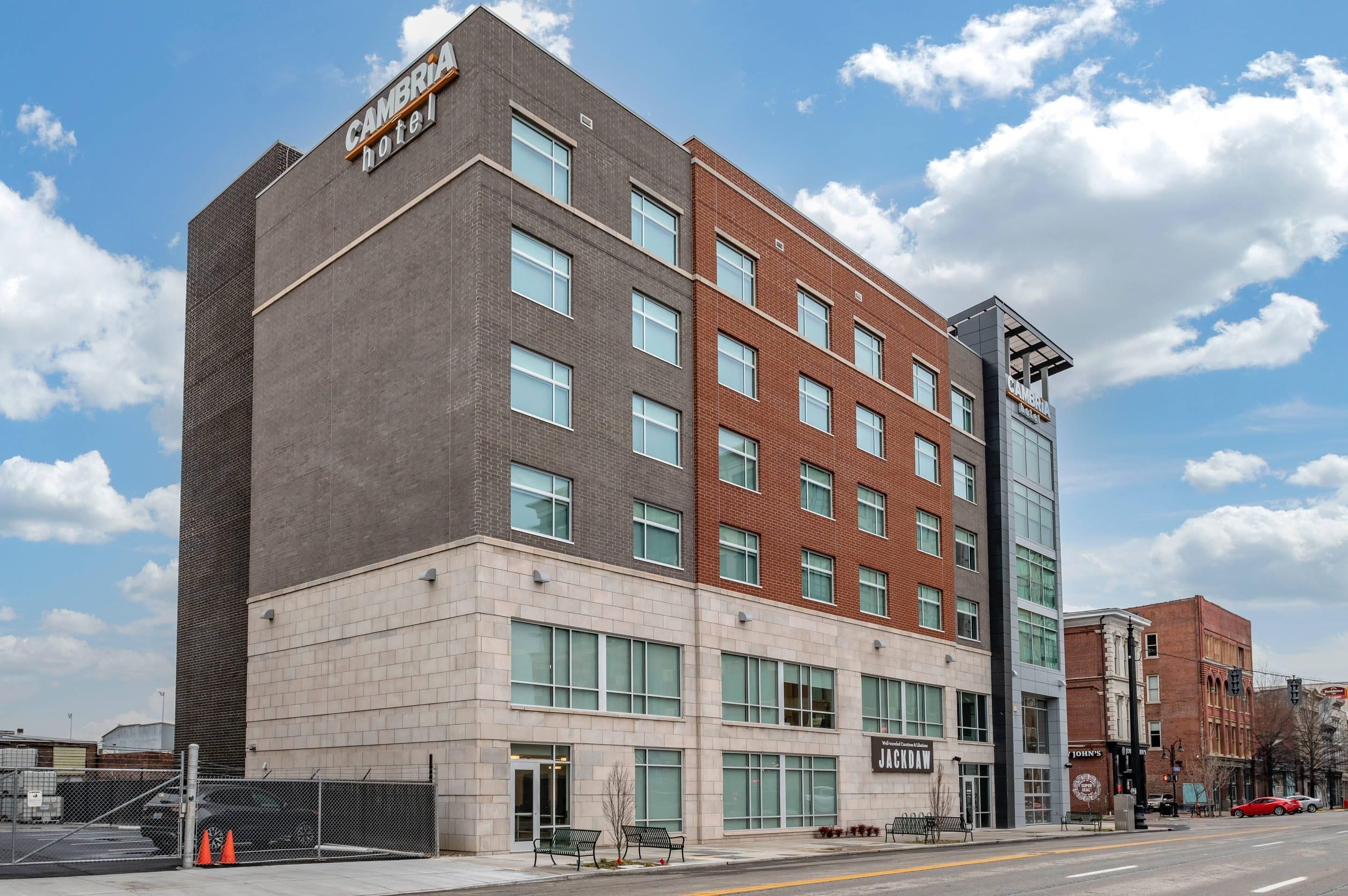 Un hotel de varios pisos con un diseño moderno, que presenta una combinación de fachadas de ladrillo y concreto, ventanas amplias y un letrero llamativo para el Cambridge Hotel.