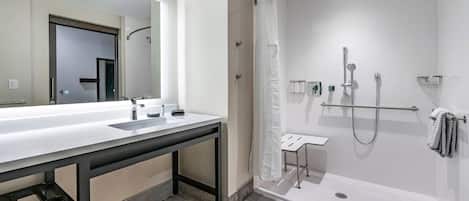 Un baño moderno con un espejo grande, un lavamanos blanco y una ducha a ras de suelo.