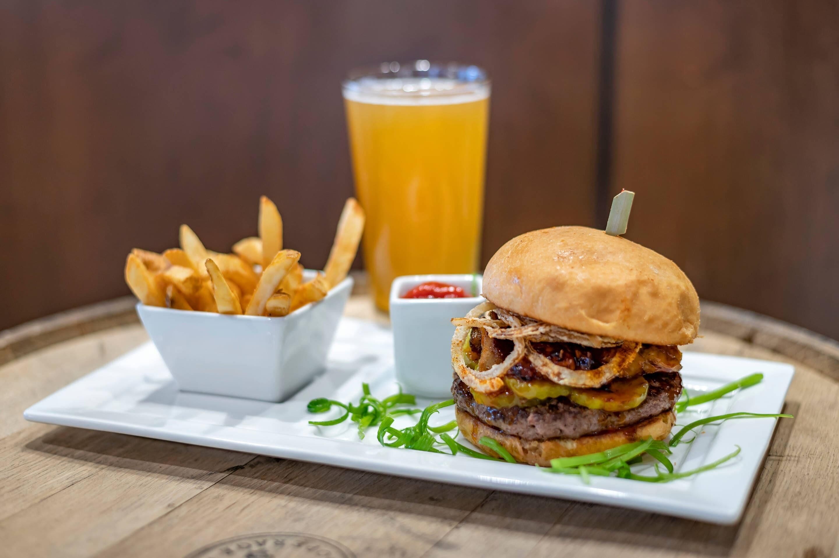Una comida que incluye una hamburguesa, papas fritas y una cerveza sobre una mesa de madera.