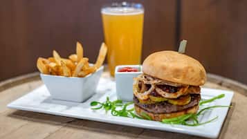 Una comida que incluye una hamburguesa, papas fritas y una cerveza sobre una mesa de madera.