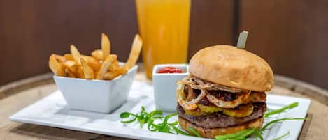 Un repas composé d’un hamburger, de frites et d’une bière, servi sur une table en bois.