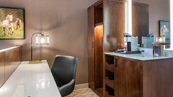 A hotel room with a wooden cabinet, a desk with a chair, a coffee maker, and a framed picture on the wall.