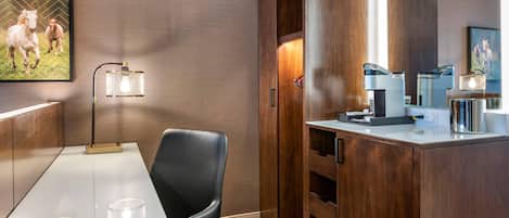 A hotel room with a wooden cabinet, a desk with a chair, a coffee maker, and a framed picture on the wall.