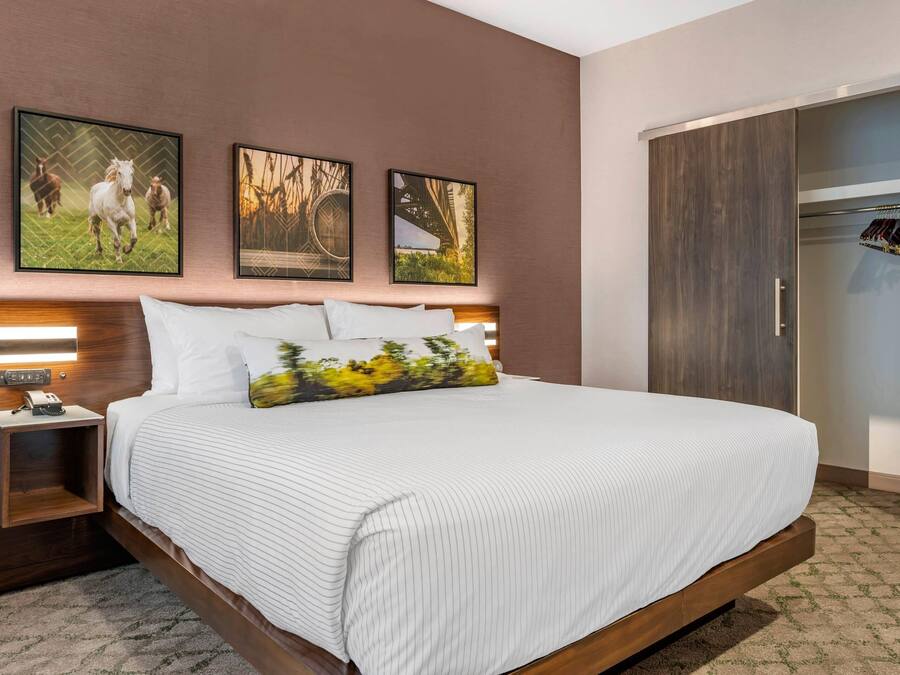 Habitación de hotel con una cama grande, cabecero de madera, mesita de noche con teléfono y armario con espejo.