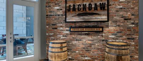 A brick wall with a sign reading "JACKDAW Coffee and Bourbon Bar" and two wooden barrels.