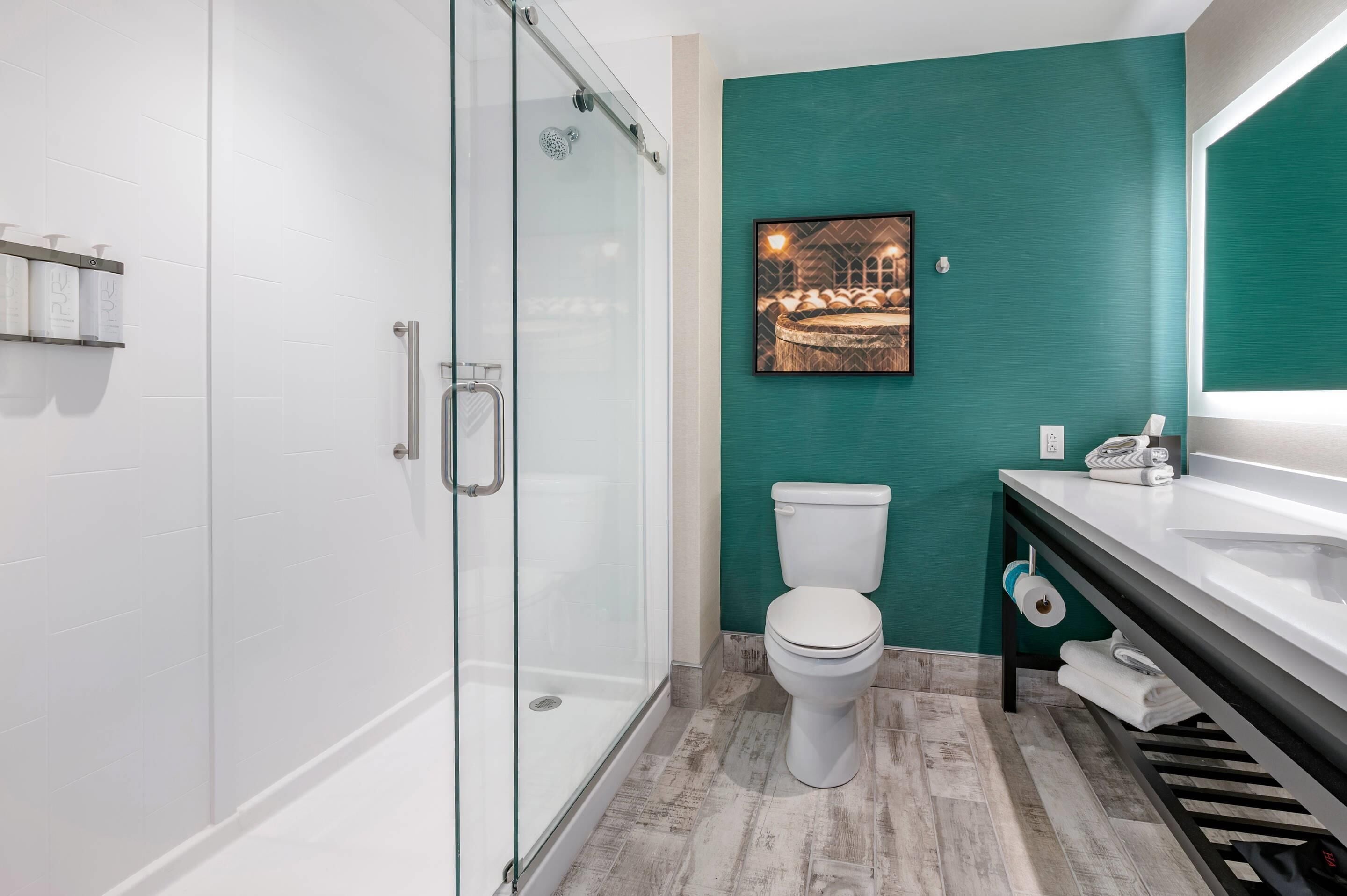 A modern bathroom with a glass-enclosed shower, a white toilet, and a teal accent wall.