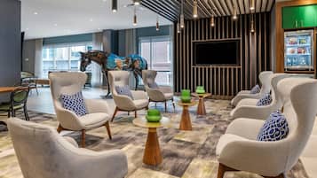 A modern lounge area with comfortable seating, a large TV screen, and a refrigerator with snacks.