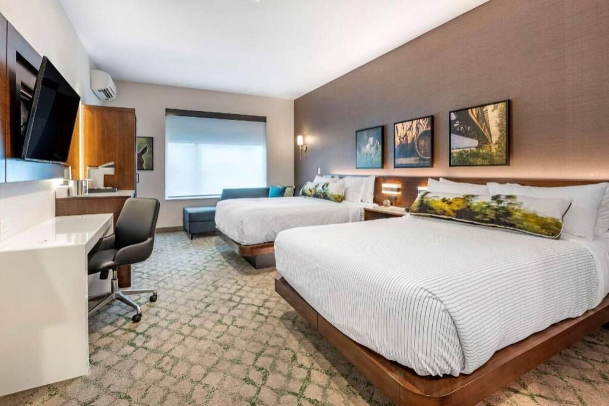 Une chambre d’hôtel avec deux lits, un bureau, une chaise, une télévision et des œuvres d’art accrochées au mur.