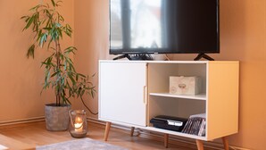 A living room with a flat-screen TV on a white cabinet, a potted plant, and a candle on the floor. - 2 Ferienwohnungen in Seenähe (Bitterfeld-Wolfen)