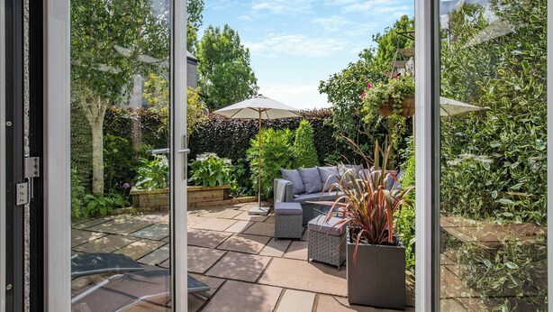 Eine Terrassenfläche mit Gartenmöbeln, einem Blumentopf und Blick auf einen Garten.