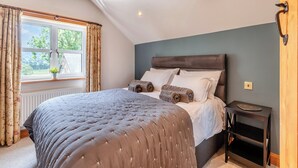 Ein Schlafzimmer mit einem großen Bett, einem Fenster mit Vorhängen, einem Nachttisch und einer wandmontierten Lampe.
