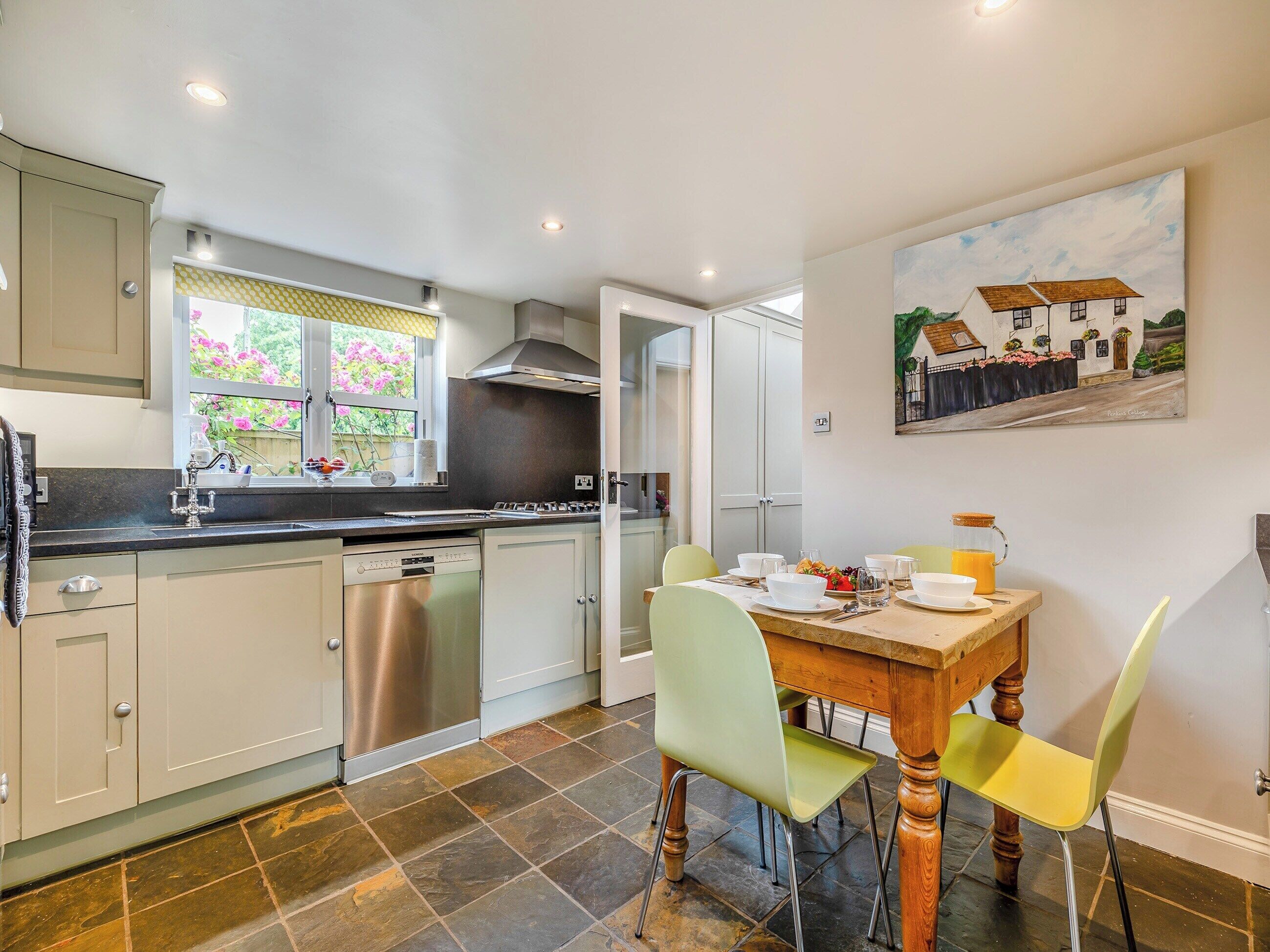 A modern kitchen with a dining area, featuring a large window, stainless steel appliances, and a painting on the wall.