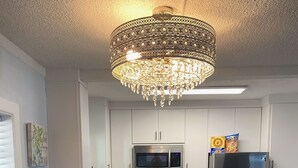 Moderni keittiö, jossa on valkoiset kaapit, ruostumattomasta teräksestä valmistetut kodinkoneet ja koristeellinen kattokruunu.