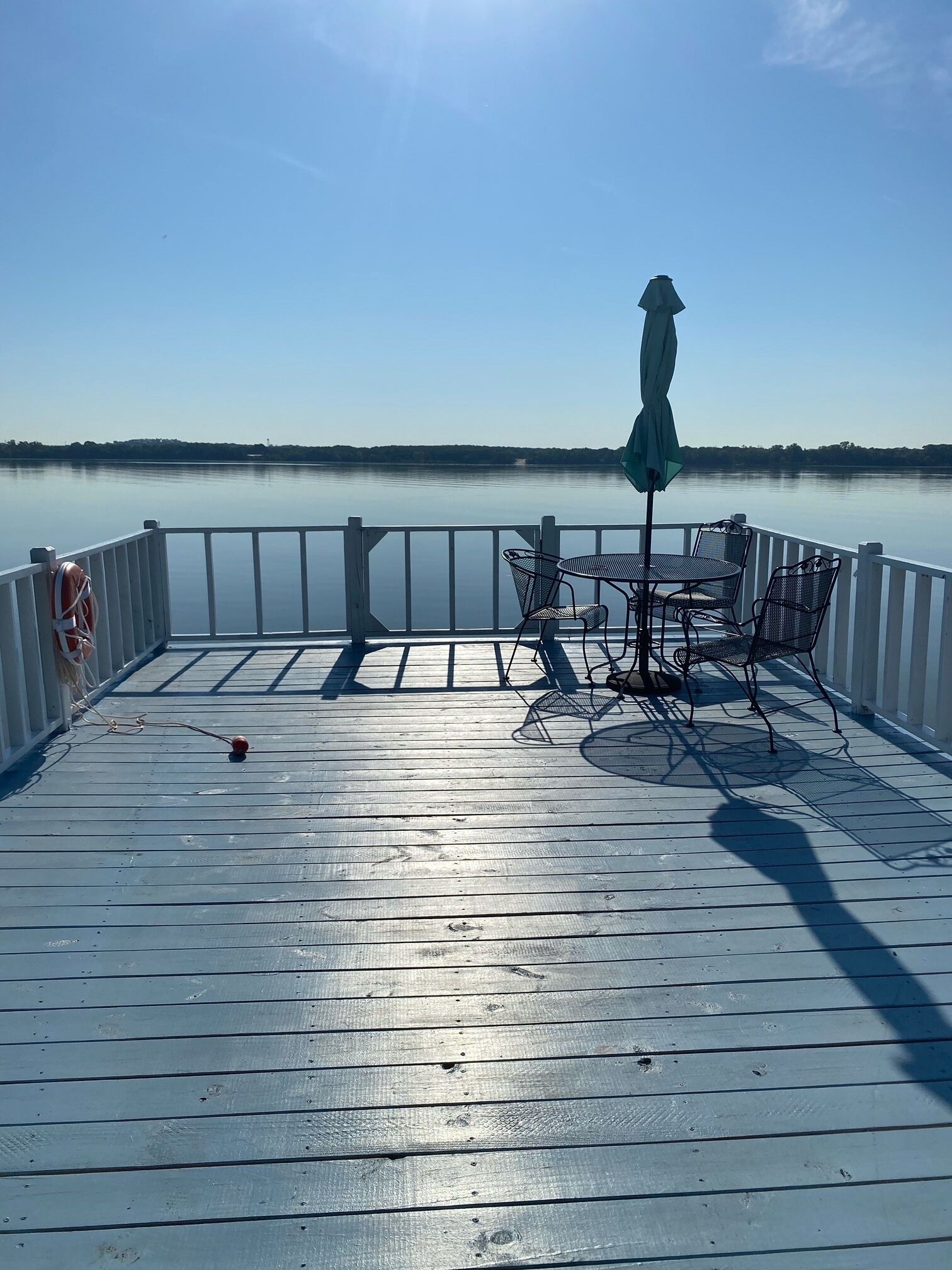 A deck with a table and chairs, overlooking a calm lake.