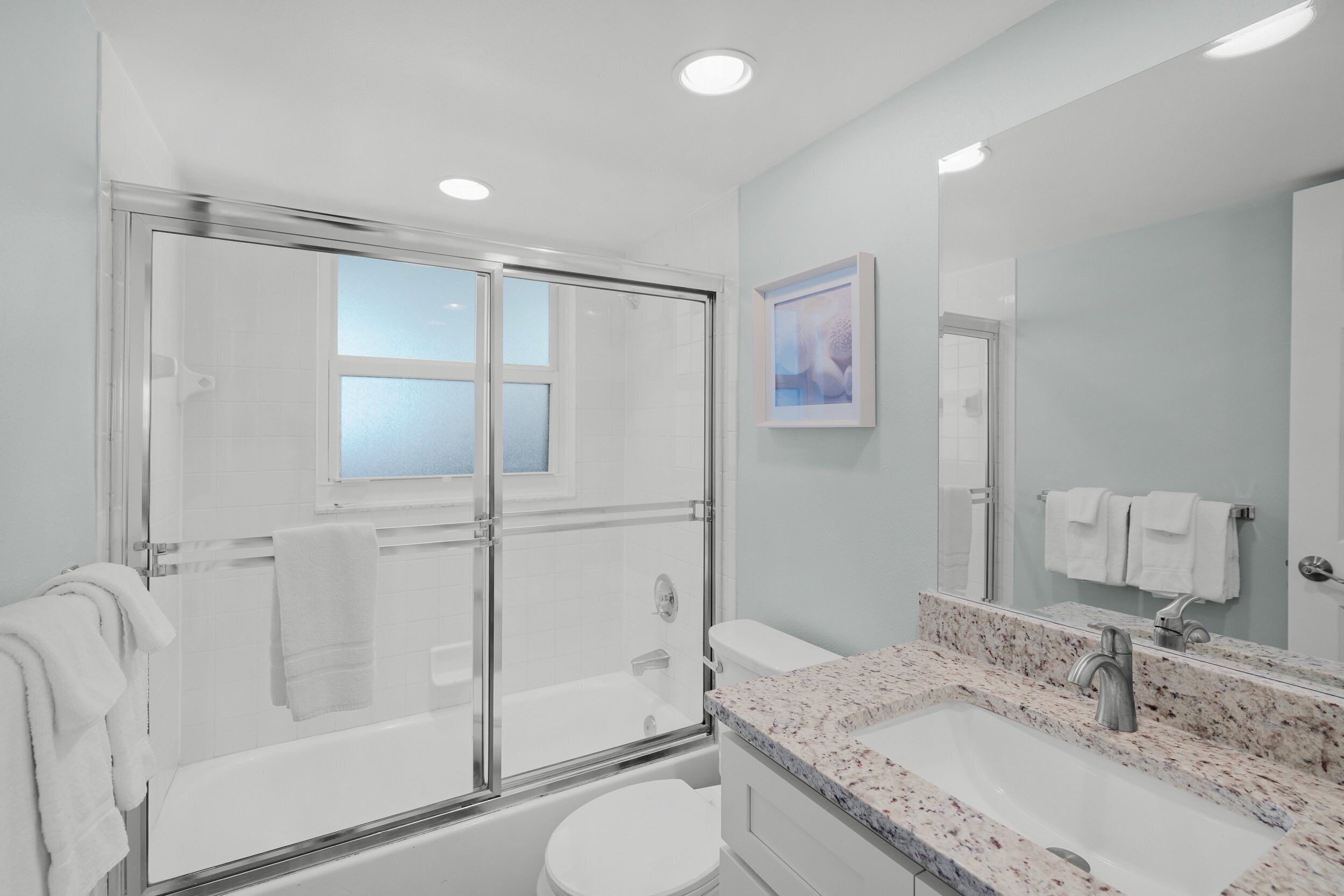 A modern bathroom with a glass-enclosed shower, a white toilet, and a granite countertop sink.