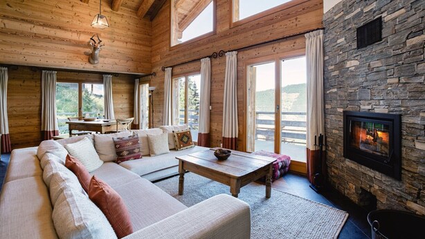 L’intérieur d’un chalet confortable, avec des murs en rondins de bois, une cheminée en pierre, un grand canapé et un coin repas.
