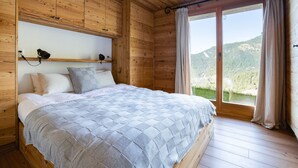 Une chambre à coucher dans une cabane en bois, avec un lit, une table de chevet, une étagère et une grande fenêtre avec des rideaux.