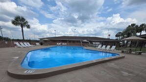 Una piscina rectangular amb un indicador de profunditat de 2,4 metres, envoltada de gandules i ombrelles, i un edifici de maó al fons.