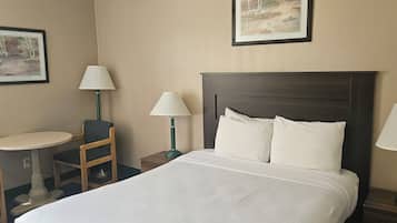 A hotel room with a bed, two bedside lamps, a chair, a small table, and two framed pictures on the wall.