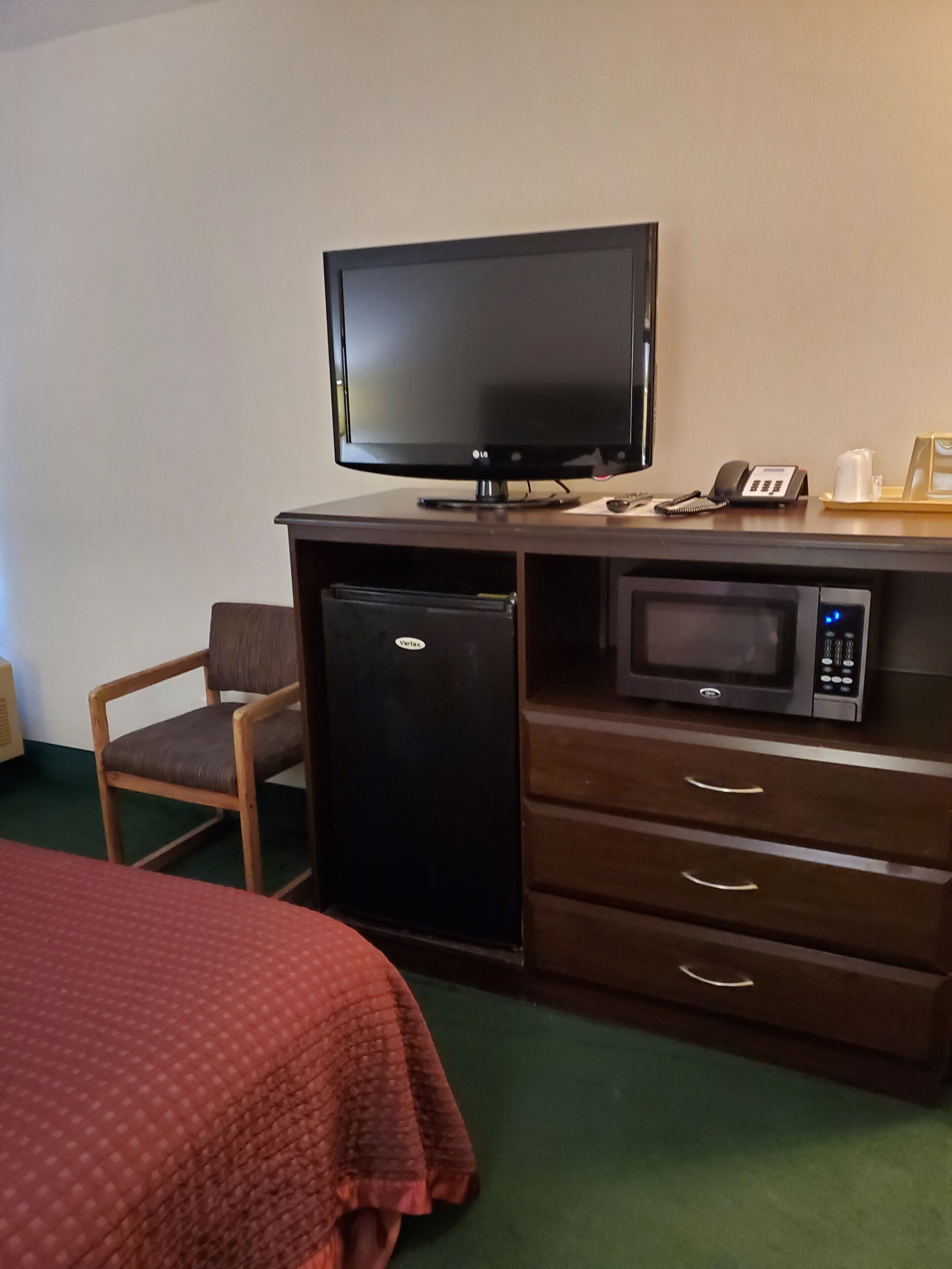 A hotel room with a bed, a desk with a television, a refrigerator, a microwave, and a telephone.