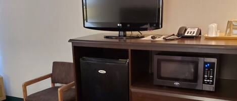 A hotel room with a bed, a desk with a television, a refrigerator, a microwave, and a telephone.