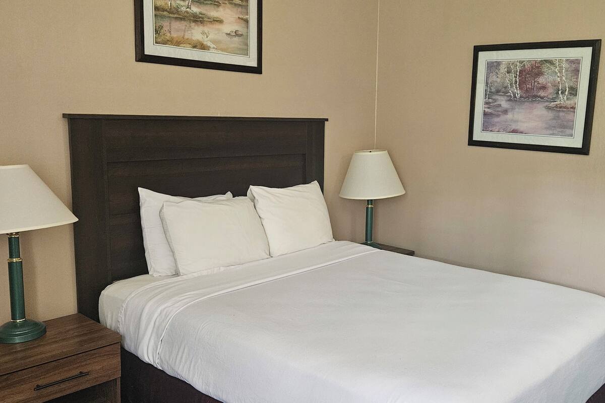 A neatly made bed with white linens, two bedside lamps, and two framed pictures on the walls.