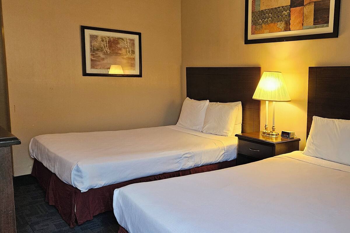 Two single beds with wooden headboards, a bedside table with a lamp, and a framed picture on the wall.