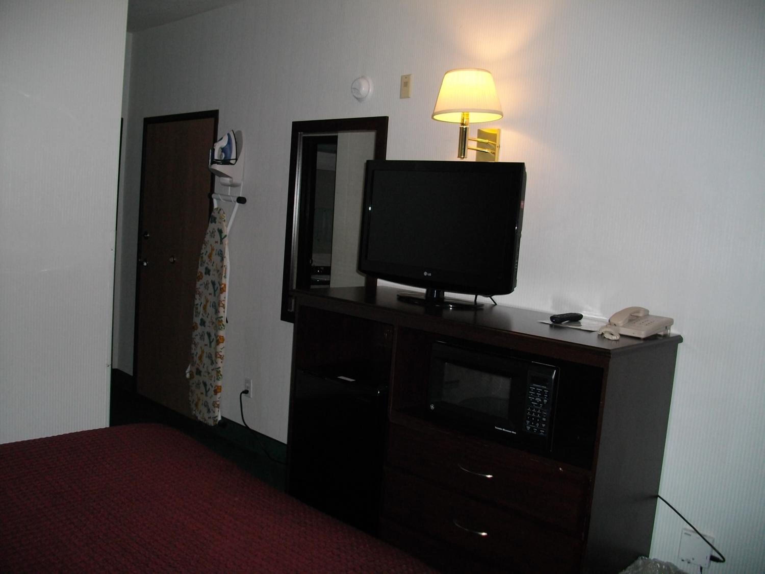 A hotel room with a bed, a flat-screen TV, a microwave, a telephone, and a lamp.