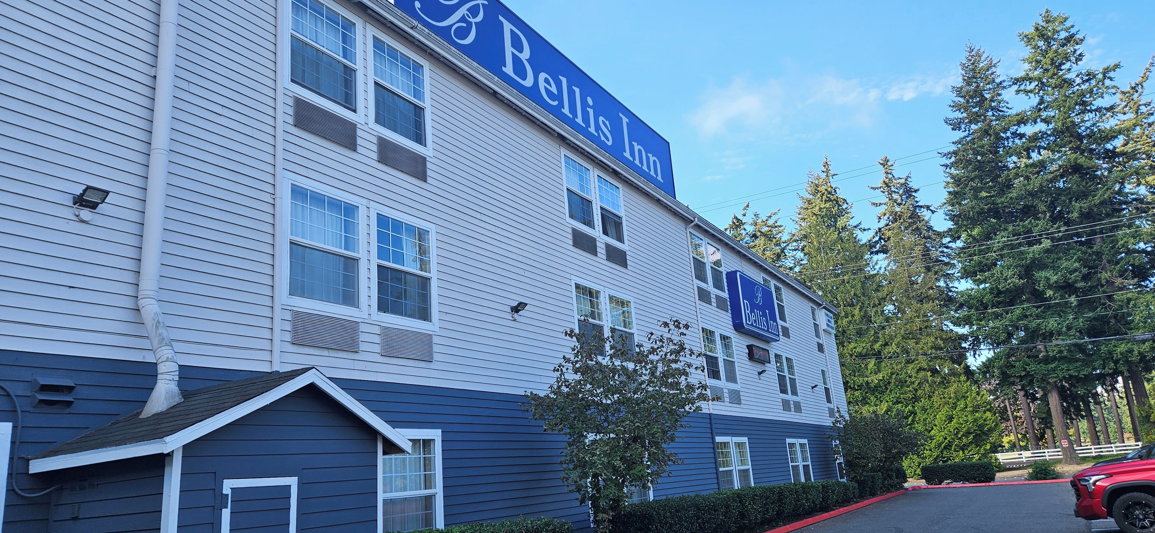A two-story hotel with a blue and white exterior, multiple windows, and a parking area with a red car.