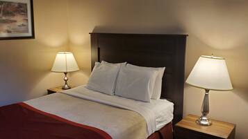 A neatly made bed with white linens and a red blanket, flanked by two bedside tables with lamps, in a room with a dark headboard and a framed picture on the wall.
