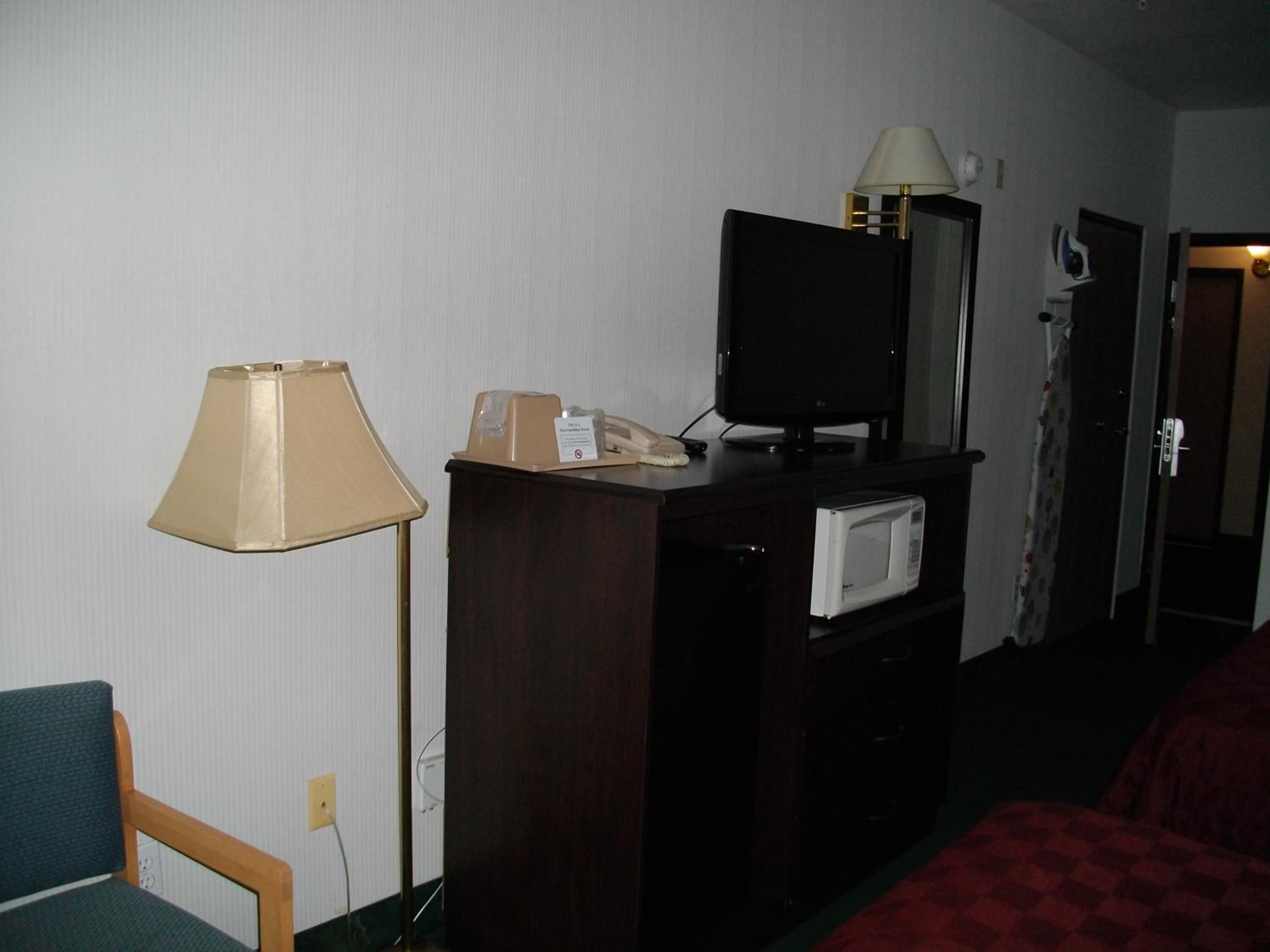 Ein Hotelzimmer mit Schreibtisch, Lampe, Fernseher, Mikrowelle und einem Bett.