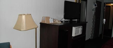 Ein Hotelzimmer mit Schreibtisch, Lampe, Fernseher, Mikrowelle und einem Bett.