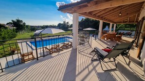 Eine überdachte Terrasse mit Pool, Liegestühlen und einer Bar.