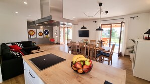 Eine moderne Küche mit Kochinsel, Essbereich mit Holzkstühlen und ein Wohnzimmer mit schwarzem Sofa.