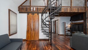 A spacious living area with a wooden floor, a curved staircase, and a sofa. - The Church (Hendersonville)