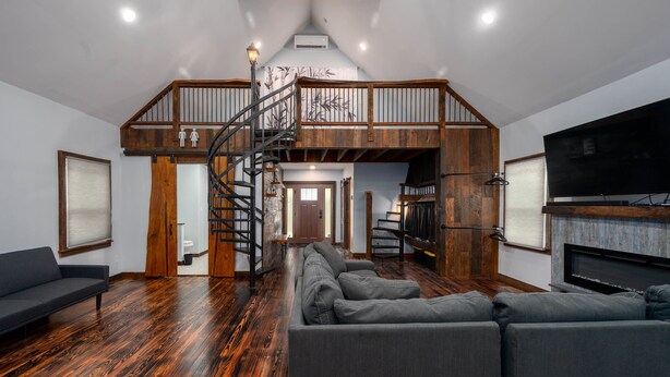 A spacious living room with a large gray sectional sofa, a wooden staircase, and a flat-screen TV mounted on the wall. - The Church (Hendersonville)