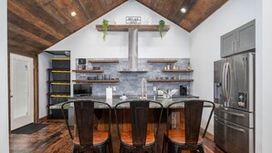 A kitchen with a central island, bar stools, a stainless steel refrigerator, and wooden flooring. - The Church (Hendersonville)