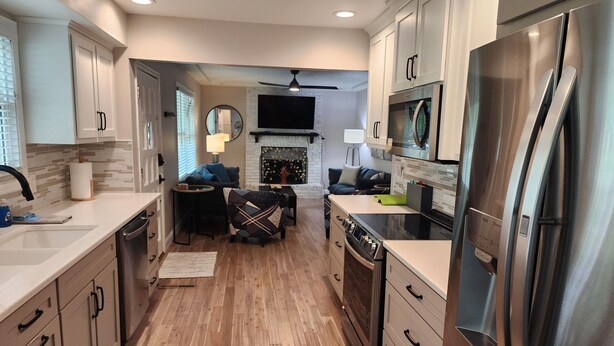 A modern kitchen with stainless steel appliances, wooden flooring, and a central island. - Renovated 3BR/2bath Ranch Near Hospital-Ideal for Families & Medical Stays (Merriam)