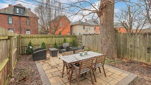 A backyard patio with a wooden table and chairs, surrounded by a wooden fence and a large tree. - Housepitality - Top Choice Flat - Great Location (Columbus)