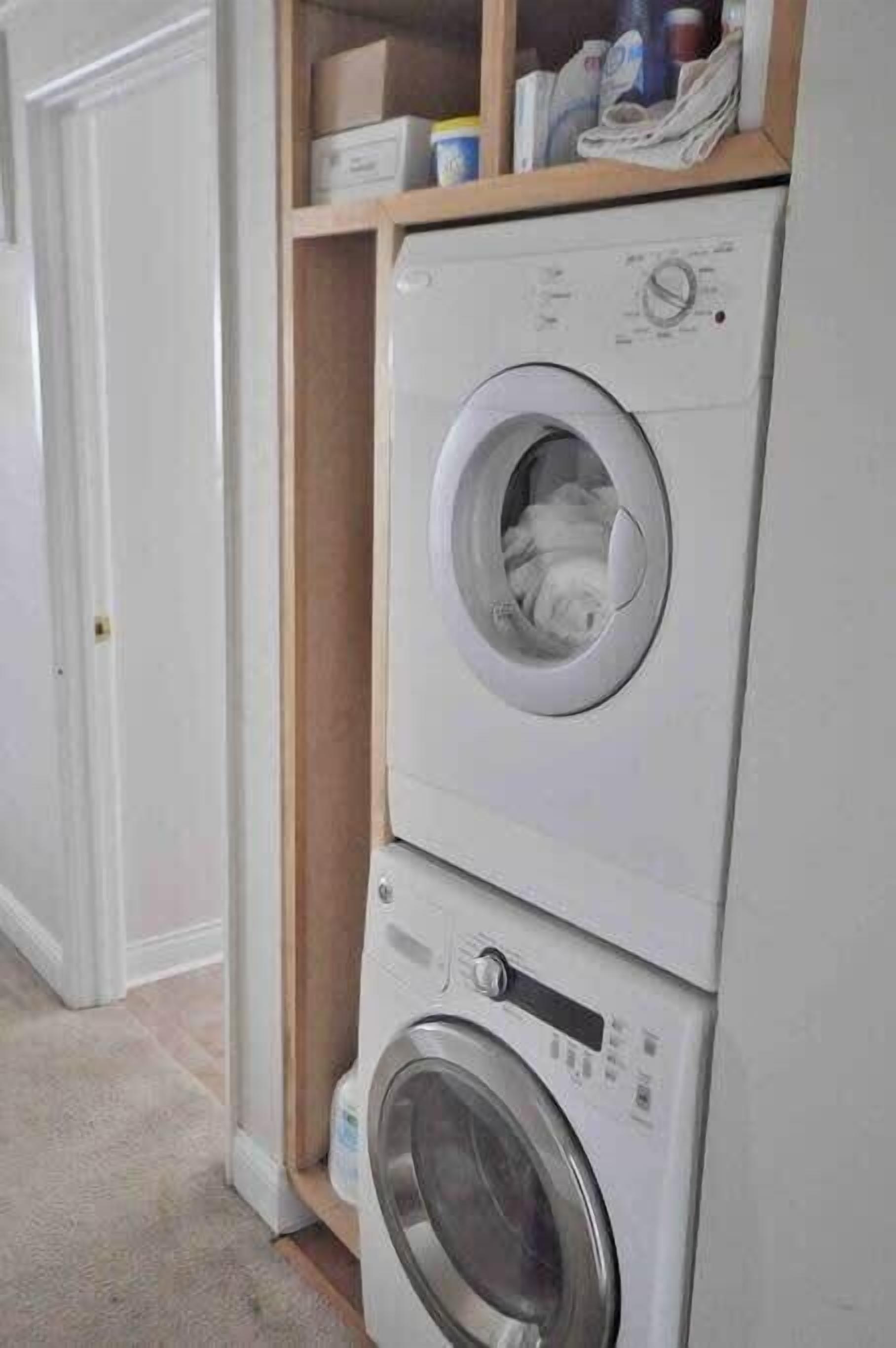 A stacked washer and dryer unit in a hallway with a wooden shelf above it containing various items.
