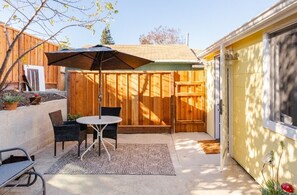 A patio with a table and chairs, a wooden fence, and a yellow garage door. - Modern cottage with full kitchen & private patio. Close to great hiking trails! (Oakland)