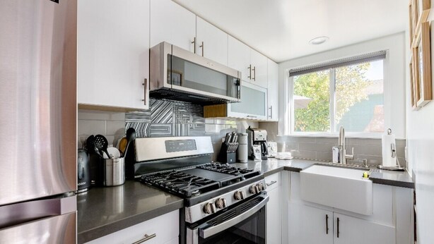 A modern kitchen with stainless steel appliances, white cabinetry, and a window providing natural light.
