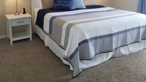 A neatly arranged bedroom with a bed, two bedside tables, a nightstand, a wall-mounted lamp, a framed picture, and a ceiling light fixture. - 2027 OPEN FOR BOOKING!  PIERVIEW 107 OCEAN-BEACHFRONT CONDO, 2BD&2BA SLEEPS 6 (Nags Head)