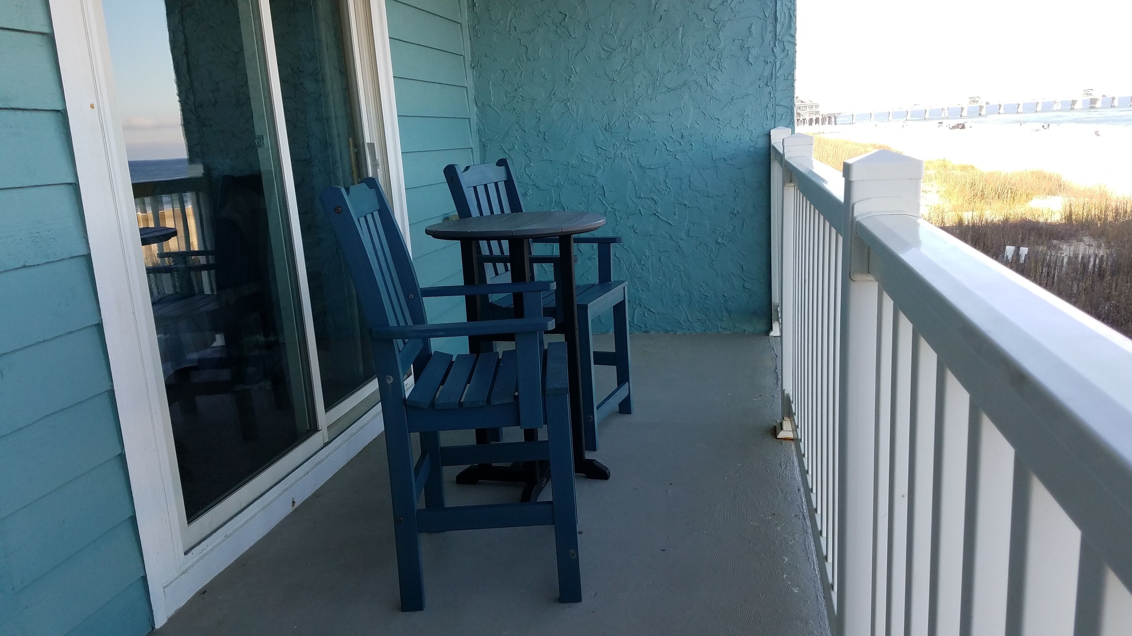 A balcony with a table and two chairs, a view of the beach, and a railing.