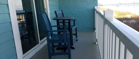 A balcony with a table and two chairs, a view of the beach, and a railing.