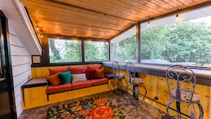 A cozy room with a wooden ceiling, a cushioned bench, a patterned rug, and metal chairs.